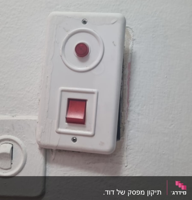 מתג חשמלי עם כפתור אדום על קיר לבן